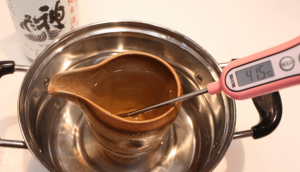 A katakuchi of sake heating up while its temperature is checked with a thermometer
